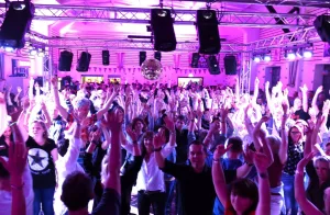 Music DJ Chris auf einer Veranstaltung vor voller Tanzfläche, Gäste mit erhobenen Händen und lachend