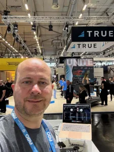 POV Perspektive vom DJ Arbeitsplatz mit Laptop und TRUE Fitness Stand im Hintergrund auf der FIBO 2026.
