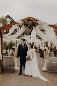 Jenny und Niklas unter dem geschmückten Holzbogen im Außenbereich des Landgasthauses Keuler in Insul